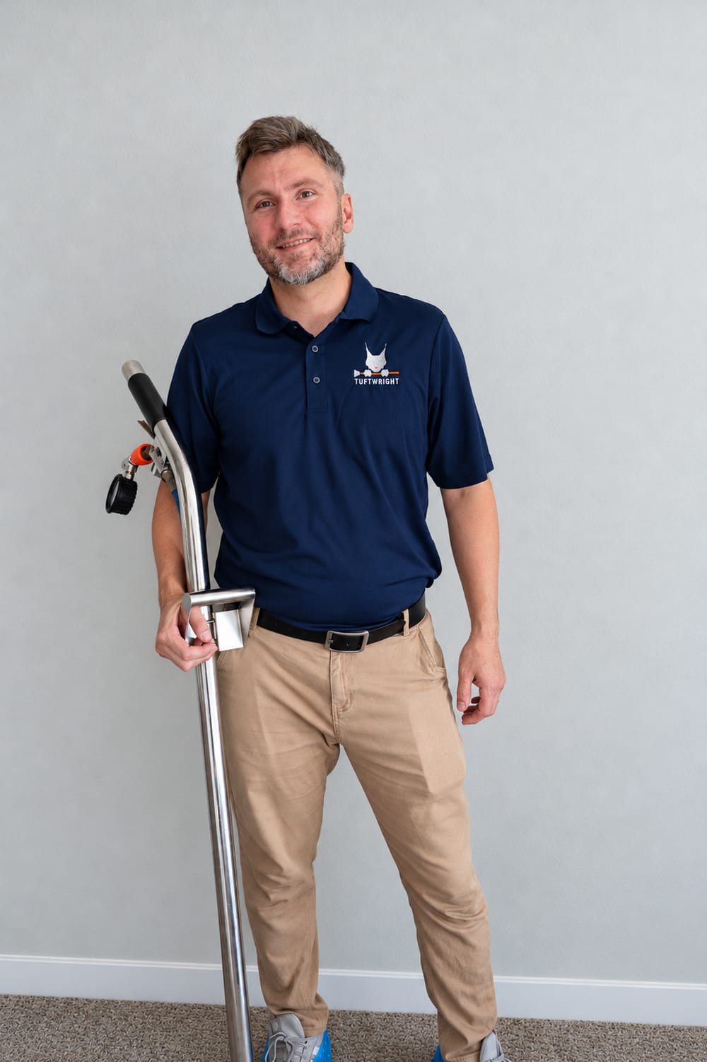 Kevin smiling at the camera in a Tuftwright polo beside his carpet cleaning wand